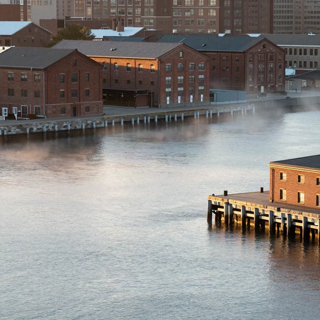 Boston Harbor at sunrise with brick waterfront buildings, mist, and calm water