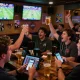 Patrons engaging in sports betting while reviewing tỷ lệ kèo nhà cái 5 at a lively sports bar, conveying excitement and social interaction.