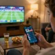 Person placing live sports bets on five88 app while watching sports in a cozy living room.