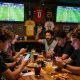 Friends enjoying Judi Bola betting experience during a live football match in a vibrant sports bar.