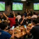 Para penggemar merayakan dan memasang taruhan pada Judi Bola di suasana bar olahraga yang energik.