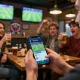 Socolive link shown on smartphone while friends cheer in sports bar during live football event